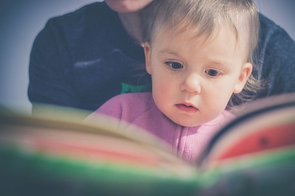 Детенце гледа во книга во рацете на родителот