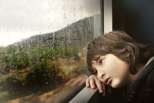 Детето потпрено на прозорец со тажен израз